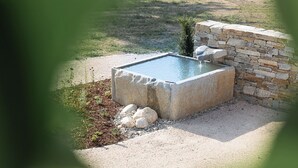 Una piscina rectangular de piedra con un muro de piedra a un lado, rodeada de grava y piedras pequeñas.