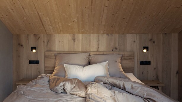 Une chambre avec un plafond en bois, un lit avec une literie beige et deux appliques murales.
