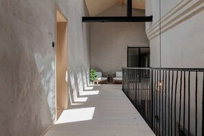 A corridor with a wooden floor, a black metal railing, and a potted plant.