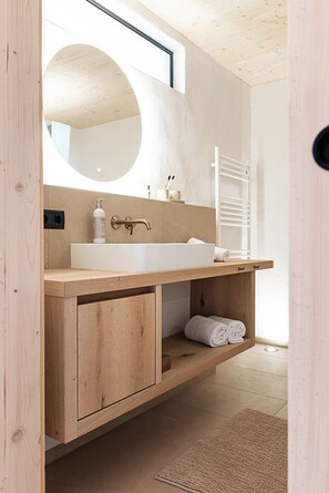 A modern bathroom with a wooden vanity, a large mirror, and a towel rack.