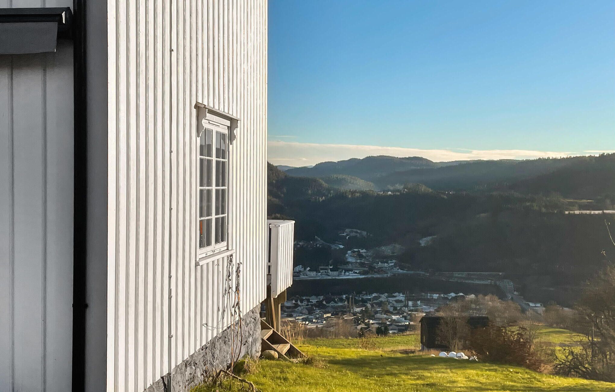 A white building with a window overlooking a valley with a town and mountains.