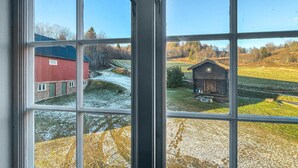 A view through a window of a rural landscape with a red barn and a wooden cabin. - 4 bedroom cozy home in Svorkmo (Svorkmo)