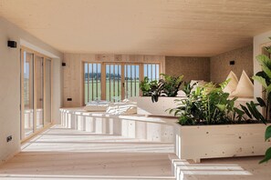 A modern interior with a wooden floor, a sofa set, and a large window with a view of greenery.