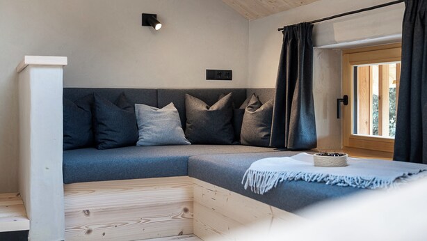 A modern, cozy room with a sectional sofa, a wooden floor, a small table with a bowl, and a window with curtains. - Ferienwohnung 5, 60qm (Eggstätt)