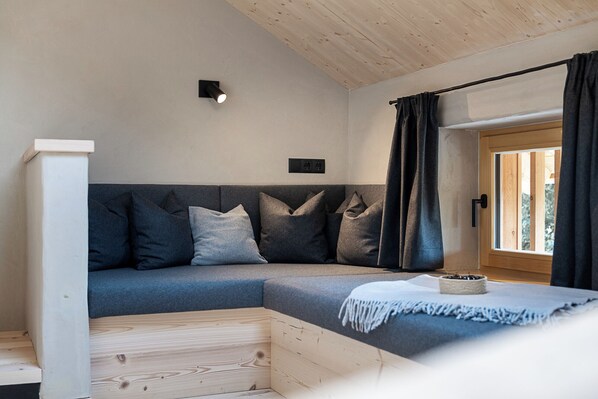 A modern, cozy room with a sectional sofa, a wooden floor, a small table with a bowl, and a window with curtains.
