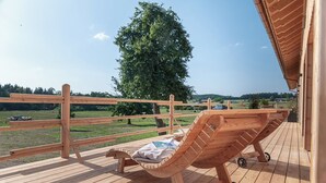 Une terrasse en bois avec un fauteuil de relaxation et une vue sur un arbre et le paysage.