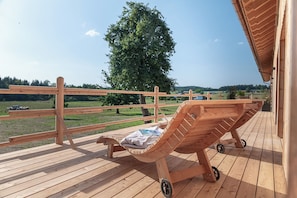 A wooden deck with a lounge chair and a view of a tree and landscape.