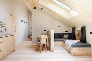 Um loft compacto e moderno, com claraboia, piso de madeira, cozinha compacta, área de estar e sofá.