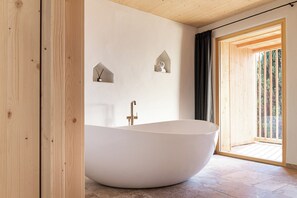 A modern bathroom with a freestanding bathtub, wooden beams, and a view of a wooden deck.