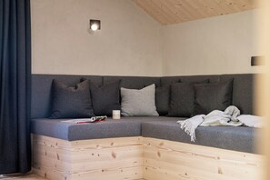 A corner room with a grey sofa, a wooden headboard, and a small wall-mounted light fixture. - Whg 7 100qm, 2 Schlafzimmer, Balkon (Eggstätt)