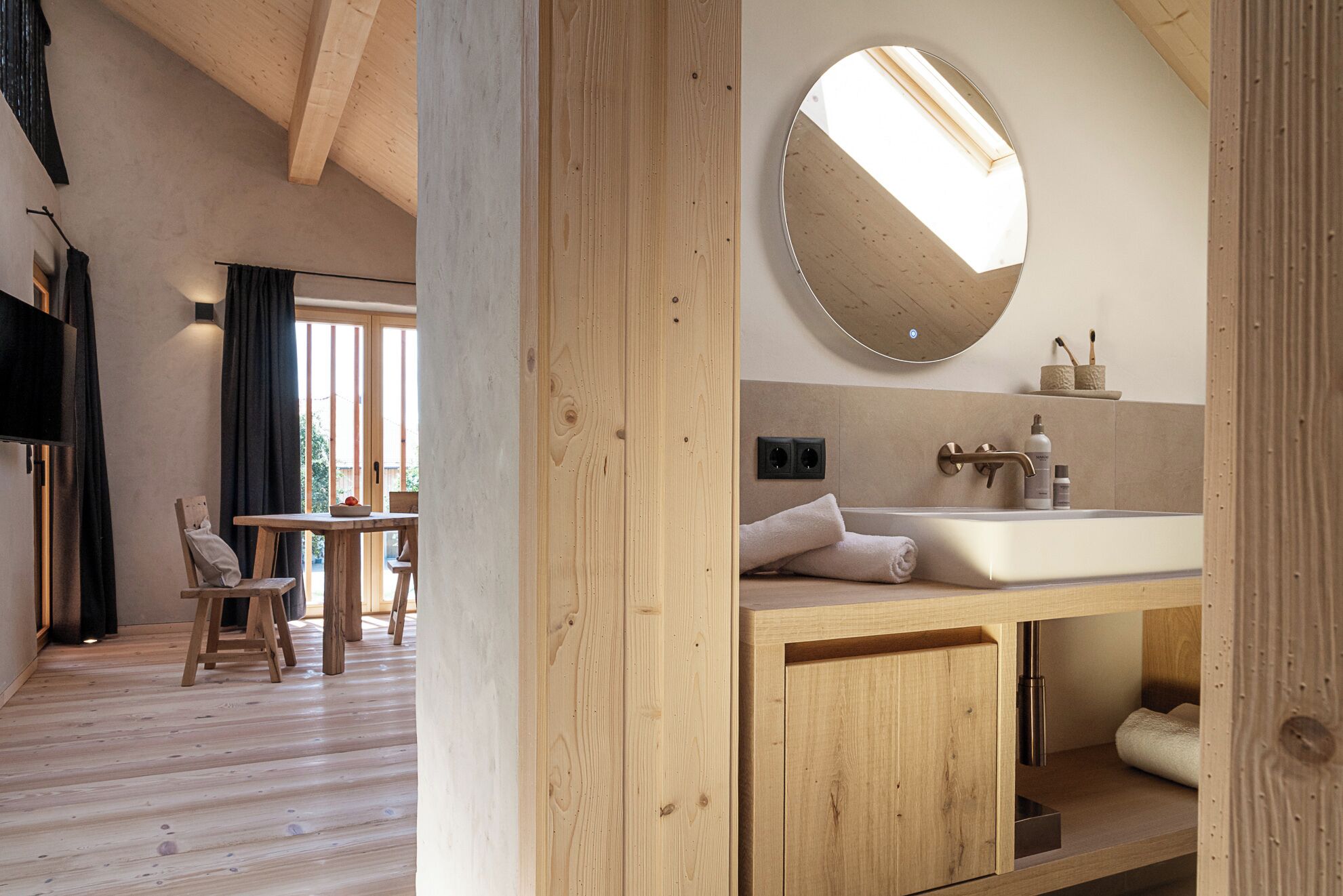 A modern bathroom with a wooden vanity, a round mirror, and a bathtub.
