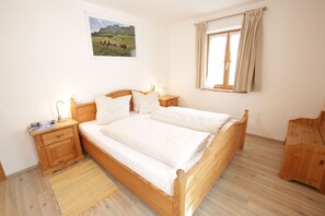 A bedroom with a wooden bed, two bedside tables, a nightstand, a window with curtains, and a landscape painting on the wall.