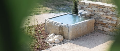 A rectangular stone pool with a stone wall on one side, surrounded by gravel and small rocks.