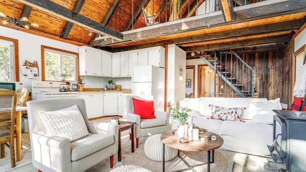 Una sala de estar acogedora con chimenea, comedor y cocina con armarios blancos.
