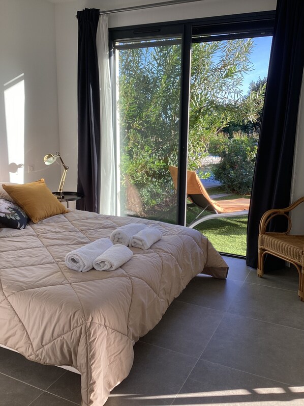 A bedroom with a large bed, a nightstand with a lamp, and a view of the outdoors through a sliding glass door.