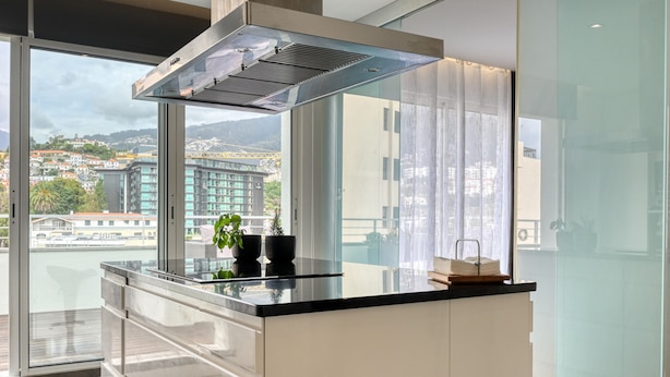 A modern kitchen with a large window, a stainless steel range hood, and a view of a cityscape.