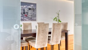 A modern dining area with a dark wooden table and beige upholstered chairs. A framed cityscape artwork is displayed on the wall above the table.