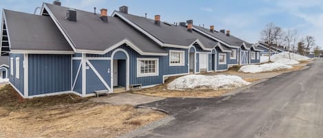 A row of blue single-story houses with attached garages, a paved driveway, and a clear sky.