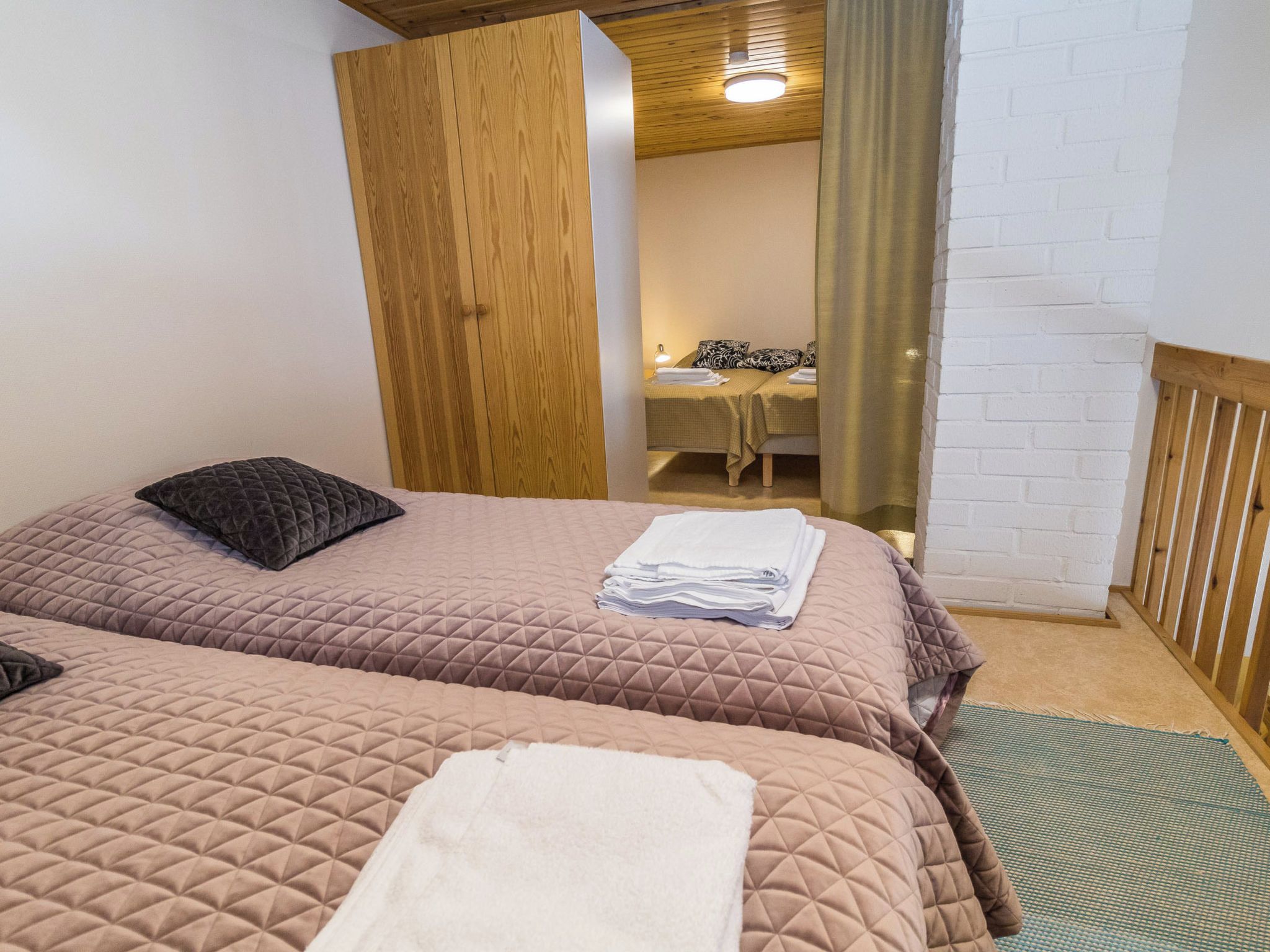 Une chambre avec deux lits, une armoire en bois, un bureau avec une chaise, et une salle de bain visible à travers une porte ouverte.