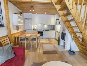 A cozy kitchen with wooden beams, a dining area with a red sofa, and a staircase.
