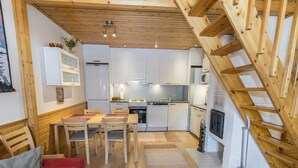 Eine moderne Küche mit weißen Schränken, eine Essecke mit einem Holztisch und -stühlen sowie eine Treppe zu einer oberen Ebene.