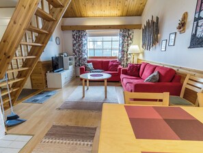 Un interior acogedor con una escalera, un sofá rojo, una mesita y un televisor.