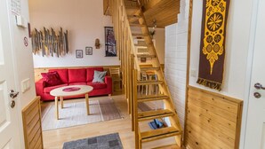 Eine Holztreppe führt zu einem Schlafzimmer im Zwischengeschoss, ein rotes Sofa und ein kleiner Esstisch befinden sich in einem modernen Wohnbereich.