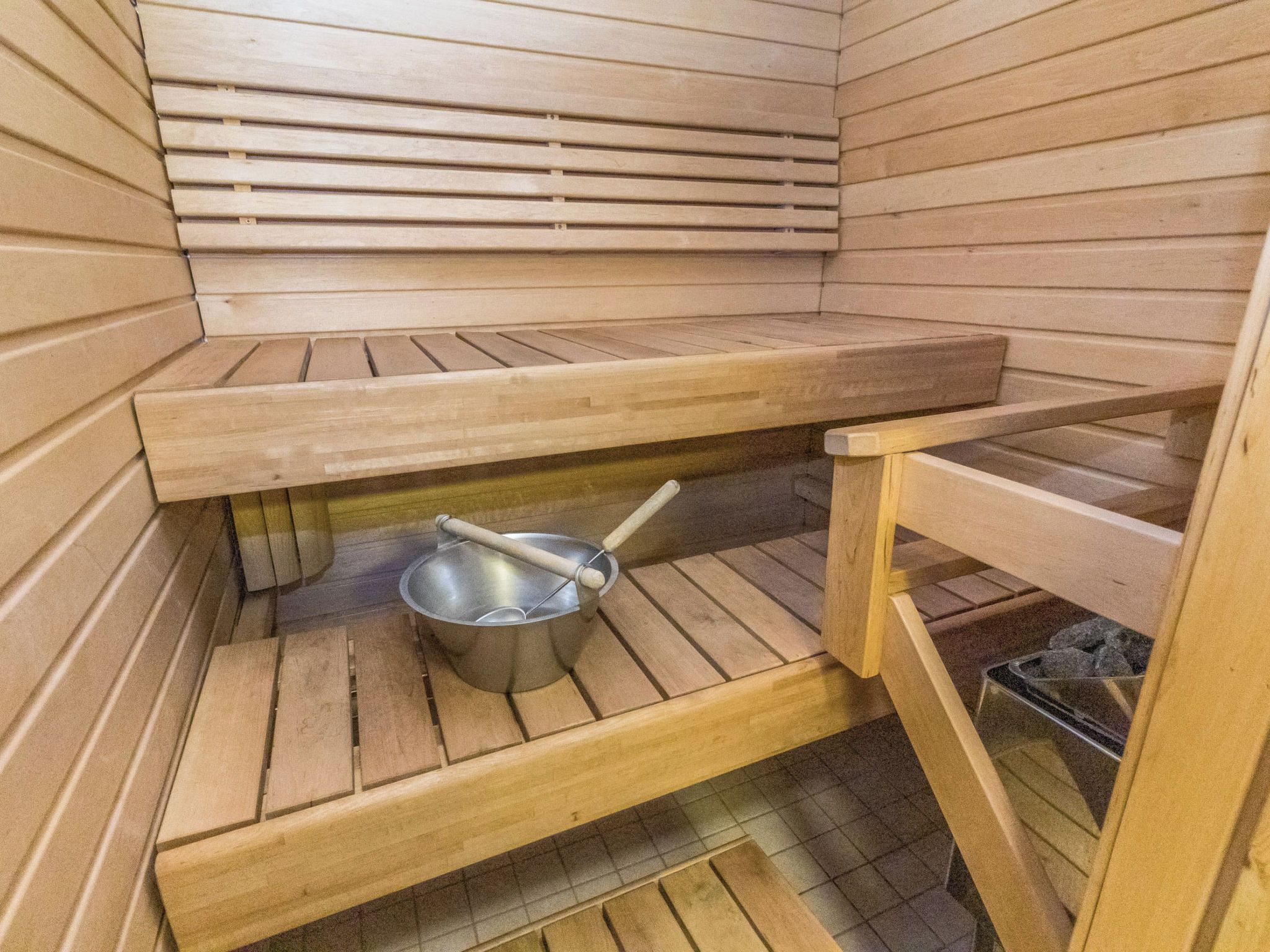 A sauna room with wooden benches and a metal basin.