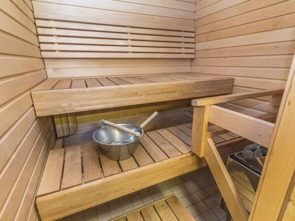 A sauna room with wooden benches and a metal basin.