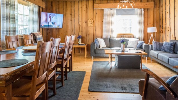 Ein gemütliches Blockhaus-Interieur mit Holzwänden, einer Essecke mit Holzbänken, einer Couch und einem an der Wand befestigten Fernseher.