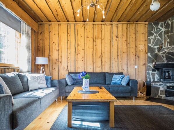 A cozy living room with wooden walls, a stone fireplace, and a modern chandelier.