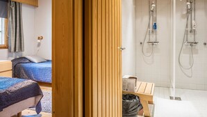 Ein modernes Hotelzimmer mit zwei Betten, einer Duschkabine und einer Holzbalkendecke.