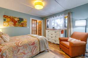 Une chambre à coucher avec un lit, une commode, un fauteuil, un tableau et une fenêtre avec des rideaux.