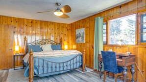 Une chambre aux murs lambrés, comprenant un lit, un bureau, une chaise et un ventilateur de plafond.