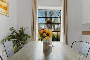 Une table à manger surmontée d’un vase en métal au style rustique contenant des tournesols, d’une plante en pot et d’une chaise en métal.