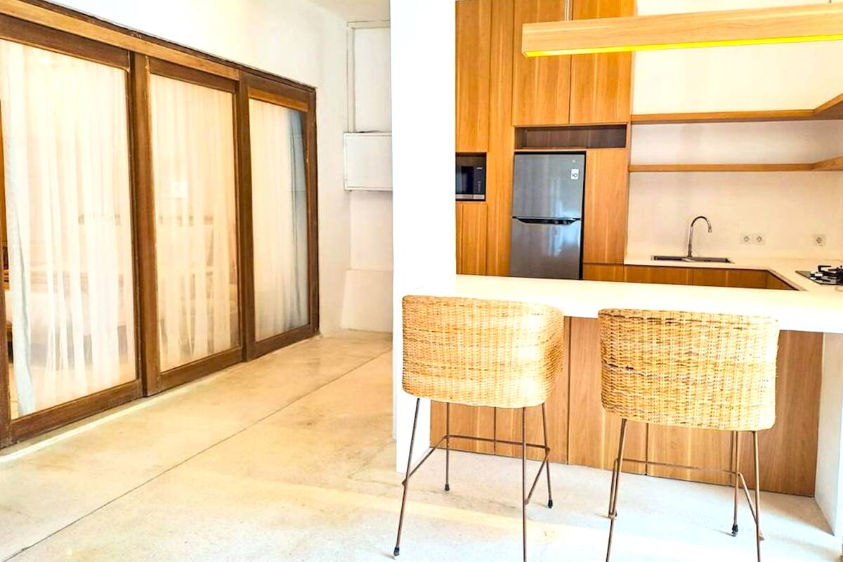 Una cocina moderna con armarios de madera, un refrigerador de acero inoxidable y dos taburetes de mimbre.