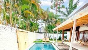 Una piscina rectangular con agua azul cristalina, rodeada por una terraza de madera y palmeras.