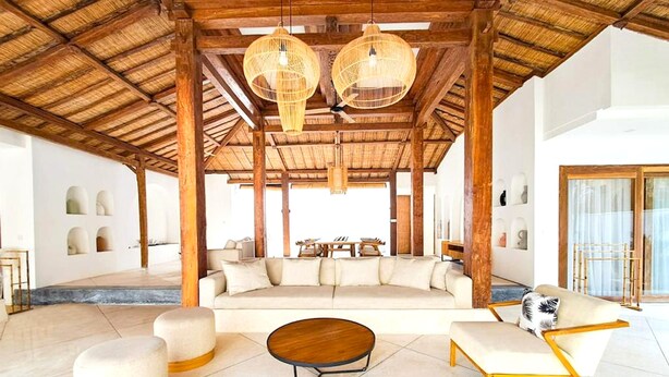 Un espacio interior amplio con techo alto, un amplio salón con sofás y una mesa de centro, y vistas al exterior.