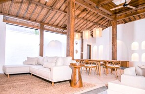 Un vaste espace de vie comprenant un grand canapé en forme de L, une table à manger en bois avec des chaises et un ventilateur de plafond.