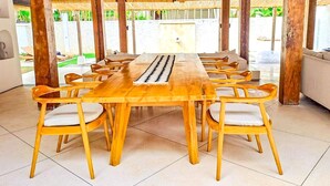 Una larga mesa de madera para comer con seis sillas, un techo tejido y vistas a la vegetación exterior.