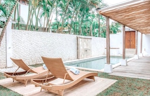 Un espace aménagé au bord de la piscine, avec deux fauteuils de relaxation en osier, une terrasse en bois et un mur en pierre.