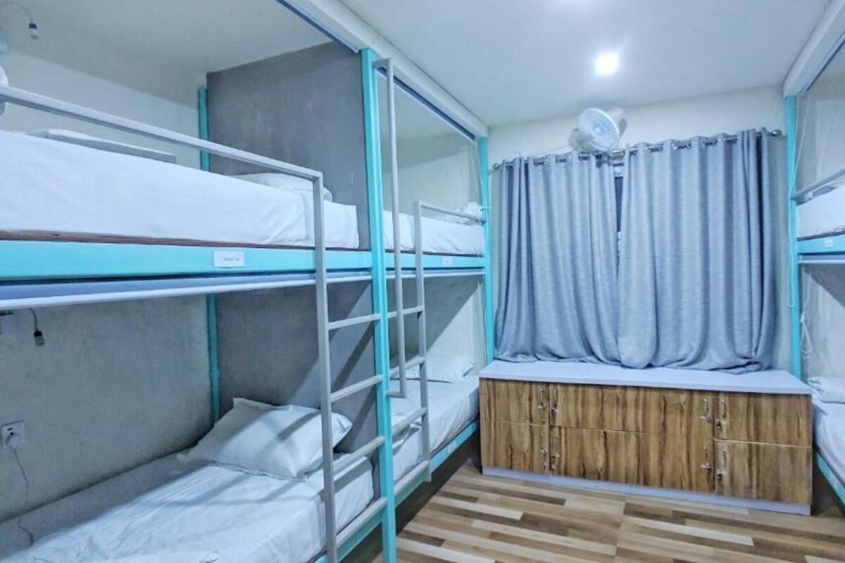 A dormitory room with bunk beds, a wooden cabinet, and a ceiling fan.
