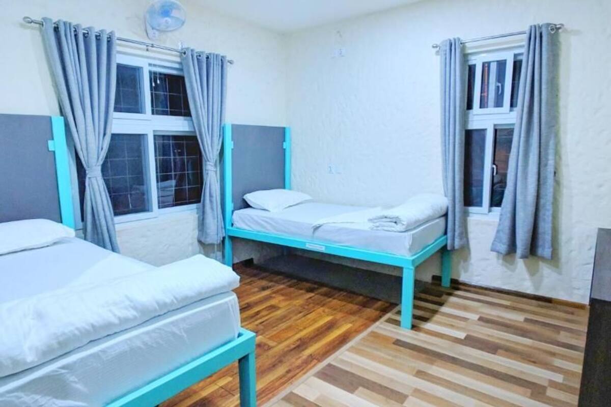 A room with two beds, wooden flooring, and curtains on the windows.