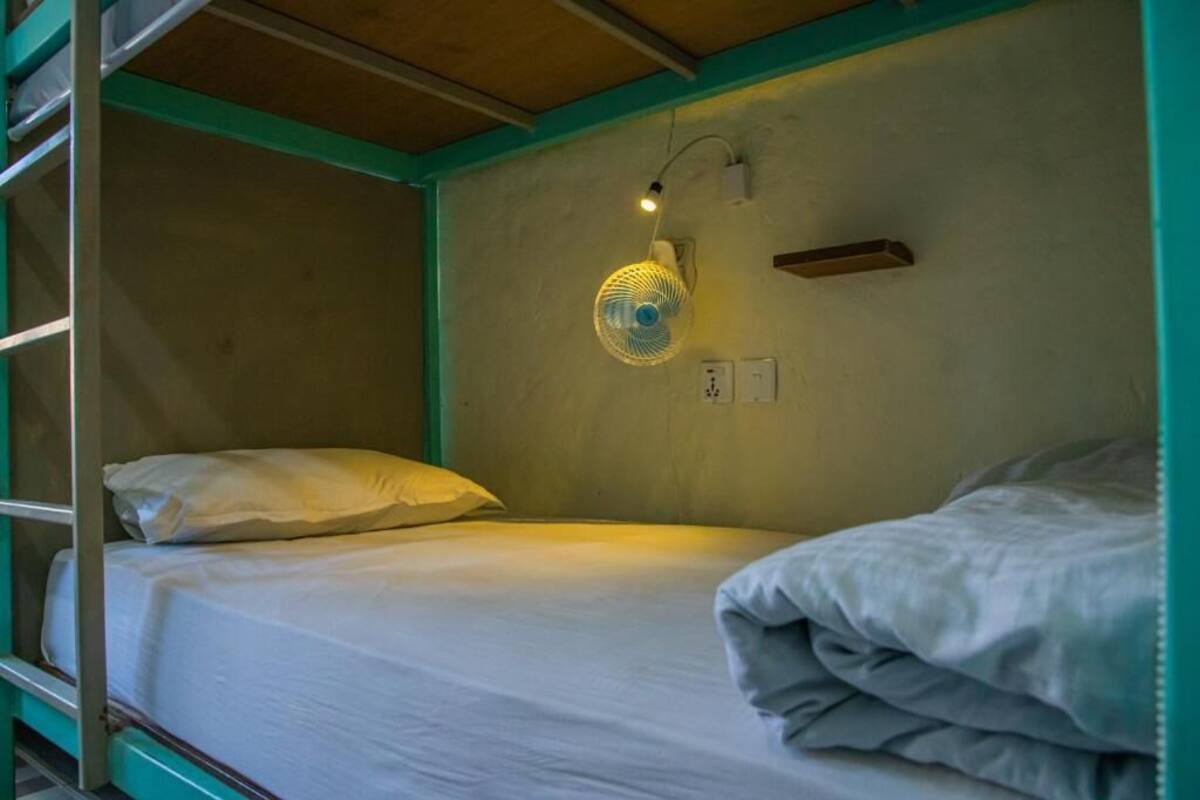 A bunk bed with a single bed on top and a lower bunk. There is a wall-mounted fan with a light on the wall above the bed.