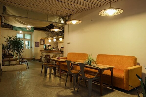 A cozy interior with a wooden table and orange sofa, a bar area, and hanging pendant lights.