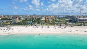 Un resort costero con varios edificios de hotel, una playa de arena con sombrillas y aguas turquesas cristalinas.