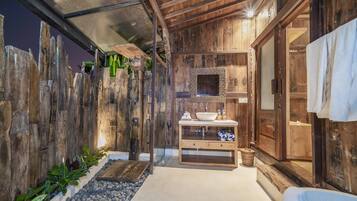 A rustic bathroom with a wooden wall, a sink with a mirror, and a towel hanging on the door.