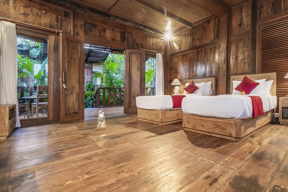 A wooden room with two beds, a nightstand, and a view of greenery outside.
