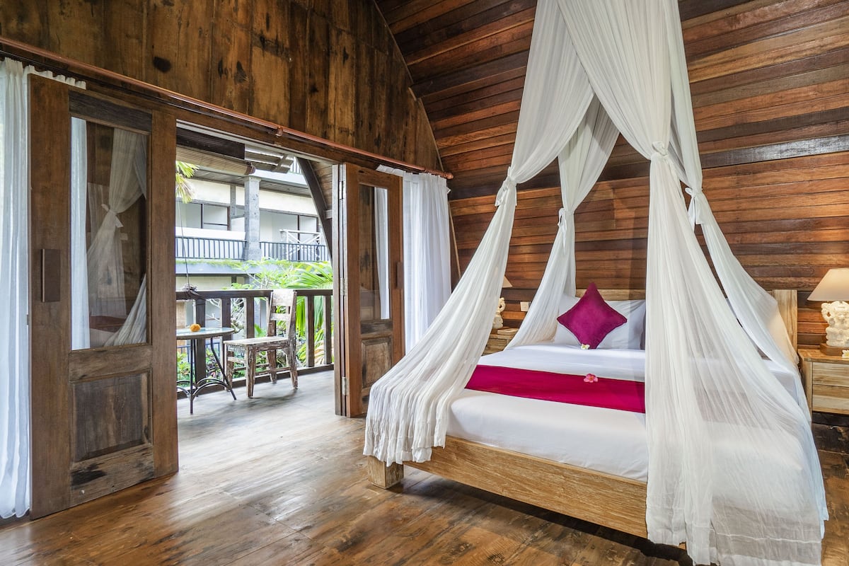 A wooden cabin-style bedroom with a four-poster bed, a nightstand, and a view of the outdoor patio.