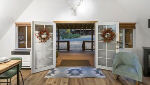 A room with a wooden floor, a green chair, a fireplace, and a deer head mounted on the wall. - A-frame cabin, fenced-in yard (Flagstaff)